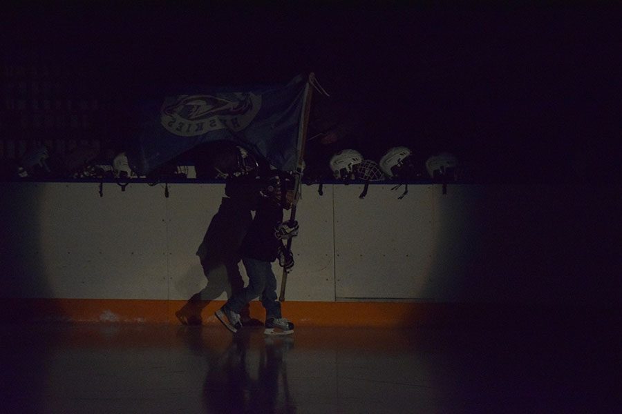 Younger hockey player goes around the rink flying the Owatonna Huskies flag.