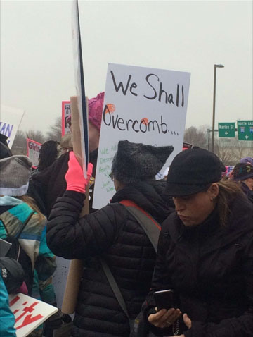 A woman holds up a sign that says we shall overcomb...