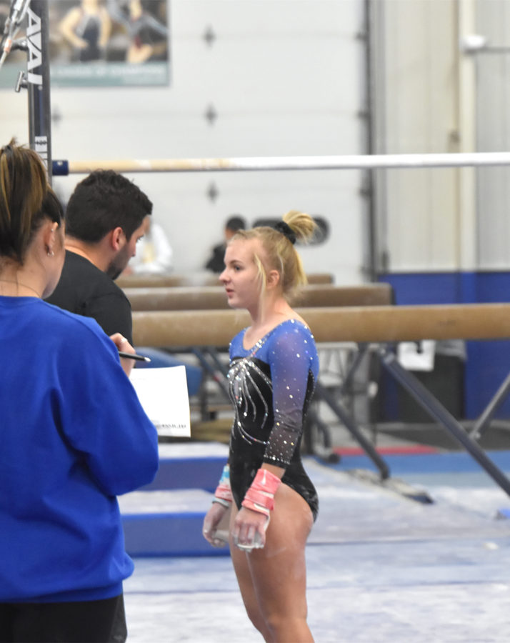 Gymnast Chloe Myer talking with head coach Evan Moe before competing on the uneven bars.