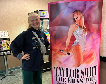 Magnet staff member Norah Sletten posing with Taylor Swift: The Eras Tour poster.