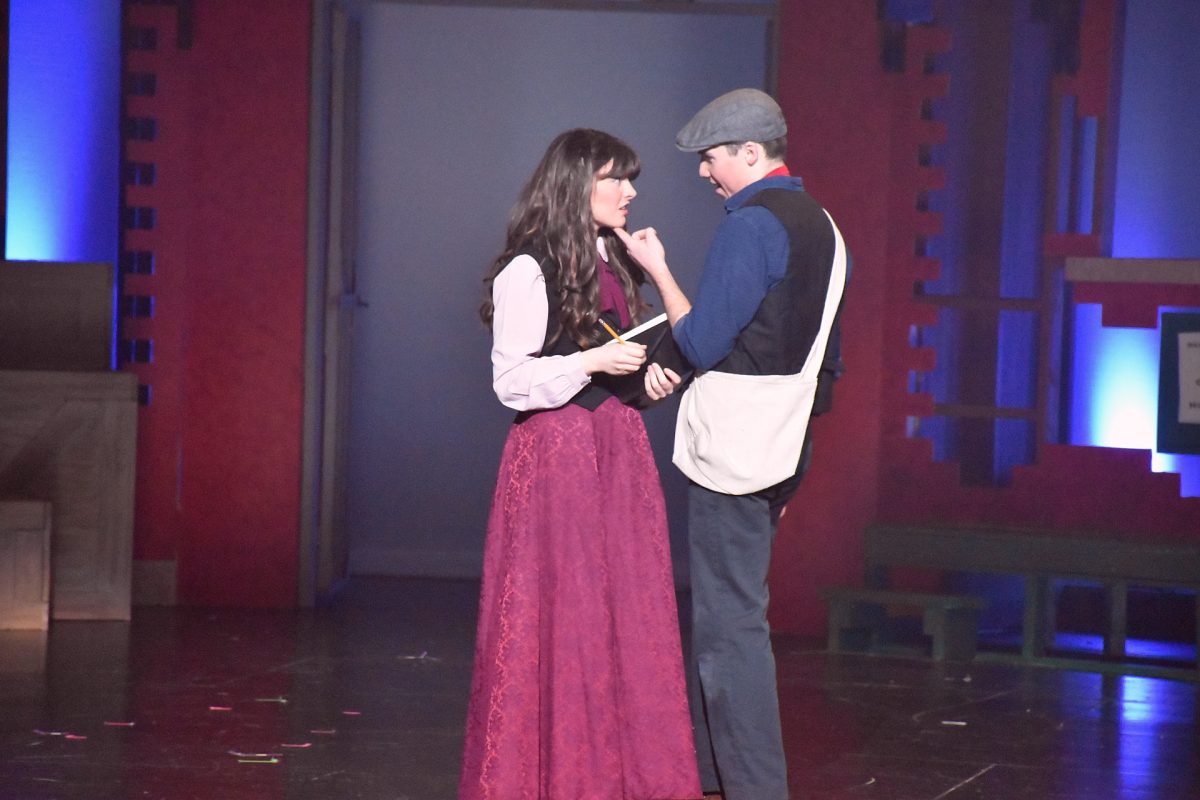 Newsies characters Katherine Plumber (Kalleigh Malecha) and Jack Kelly (Ethan Armstrong) banter on stage.