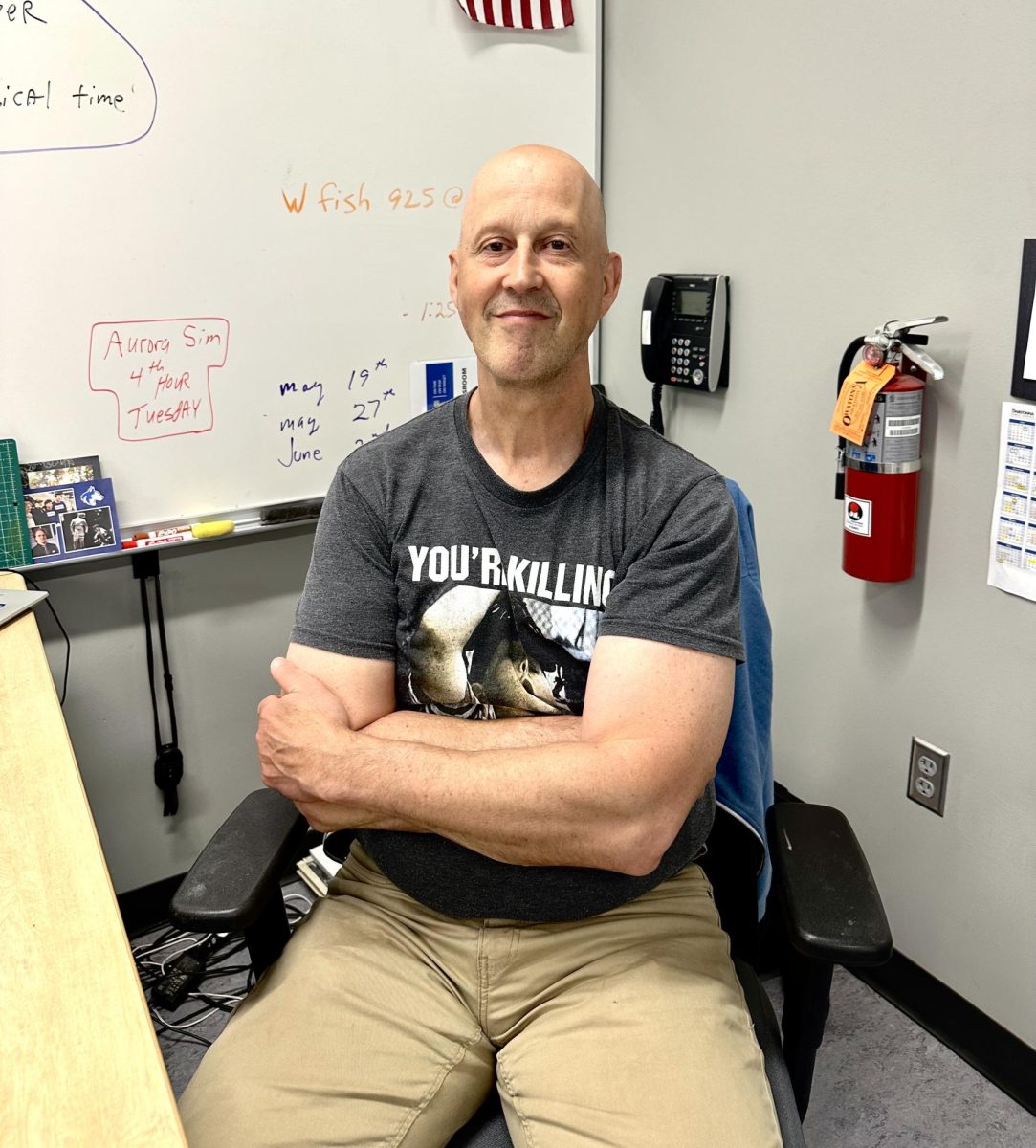 Mr, Kuehn smiles while sitting at his desk. 