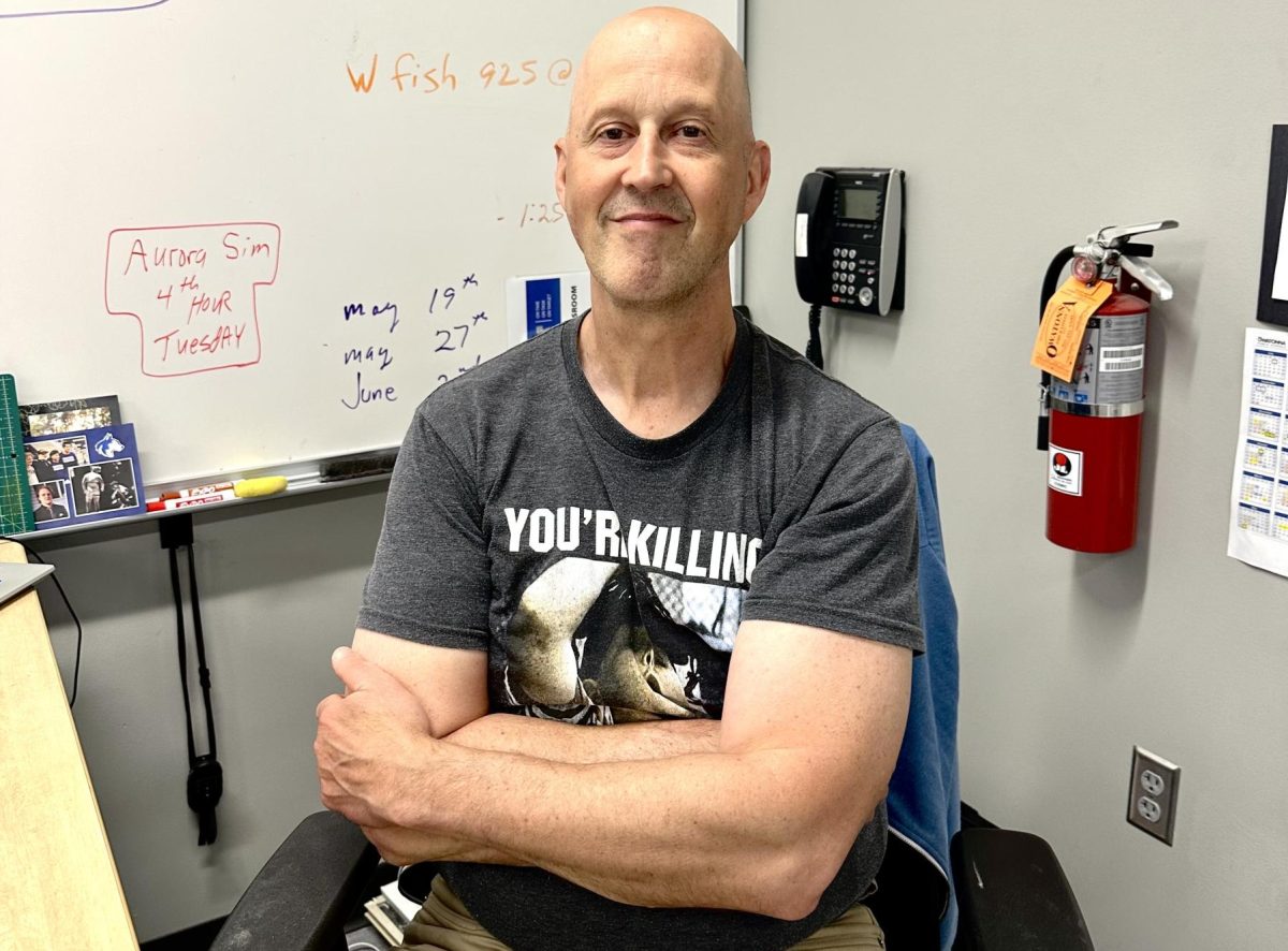 Mr, Kuehn smiles while sitting at his desk.